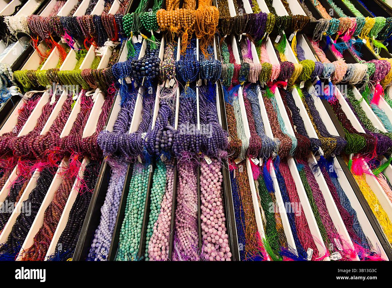 Sur un stand à plusieurs niveaux, des perles de pierres précieuses cordées de différents types sont organisées en paquets séparés. Leurs surfaces polies et leurs teintes variées brillent U. Banque D'Images