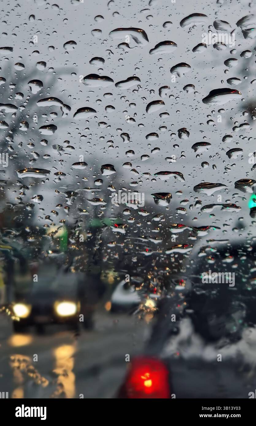 Neige fondue et gouttes de pluie sur le pare-brise d'une voiture. Vue extérieure floue, grésil en hiver comme vu par la fenêtre du véhicule Banque D'Images