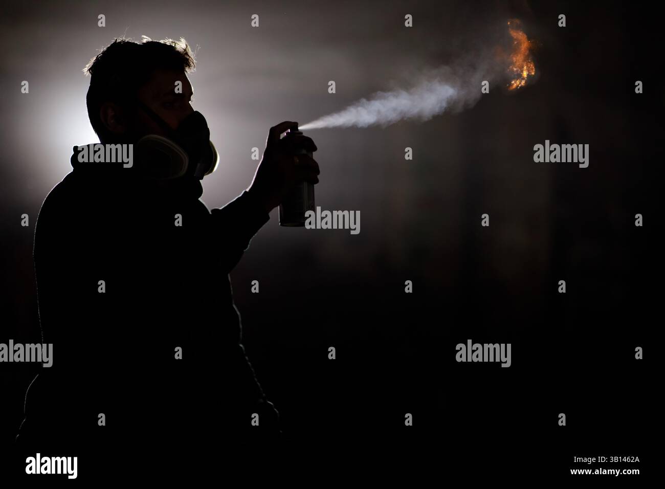 Une personne dans un masque à gaz pulvérise de la peinture dans l'air, créant un effet dramatique avec un éclat ardent. Les environnements sombres augmentent l'intensité du SC Banque D'Images