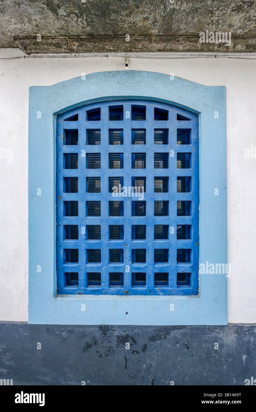 Fenêtre grillagée bleue sur un mur texturé. Mur texturé, détail architectural, façade colorée. Ce détail architectural met en valeur une façade colorée et Banque D'Images