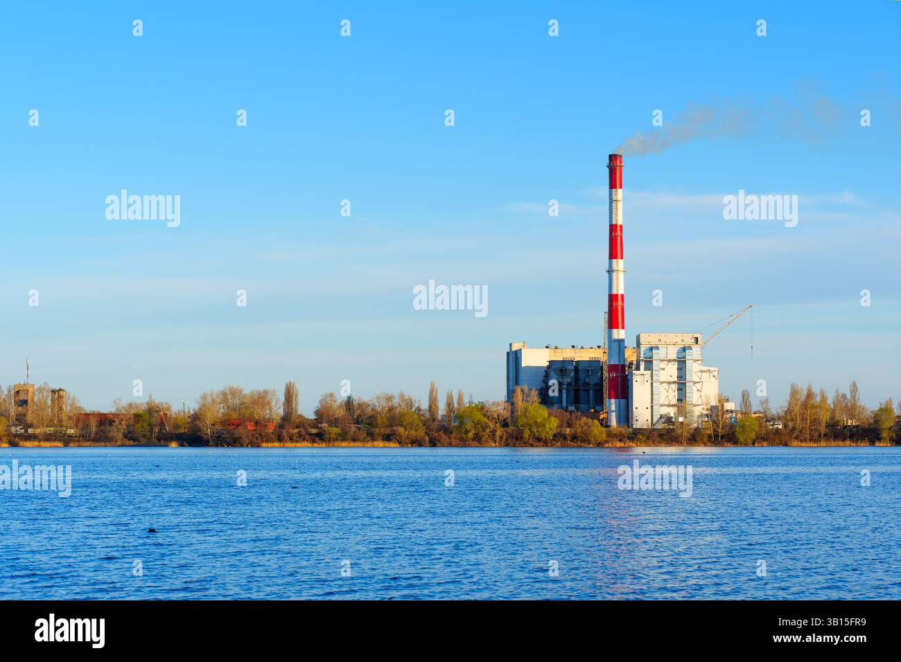L'usine d'incinération des déchets est visible sur le rivage, avec une cheminée haute émettant de la fumée, reflétant le concept de la gestion des déchets et de l'environnement Banque D'Images