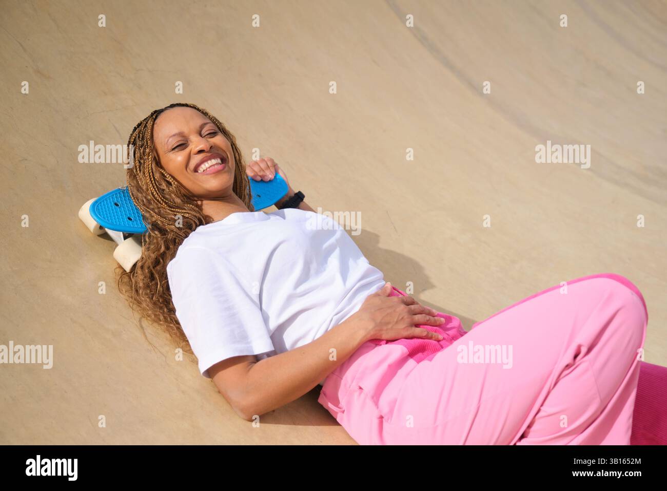 Heureux patineur allongé sur la rampe tenant la planche de penny souriant au skatepark Banque D'Images