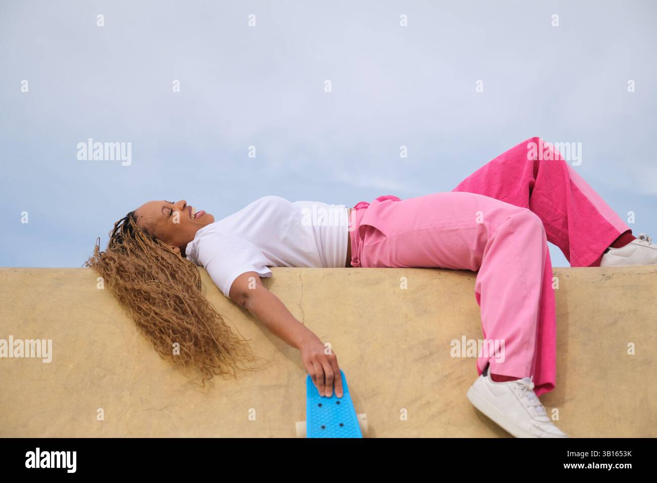 Patineur allongé sur la rampe tenant une planche à un centime profitant de la pause Banque D'Images