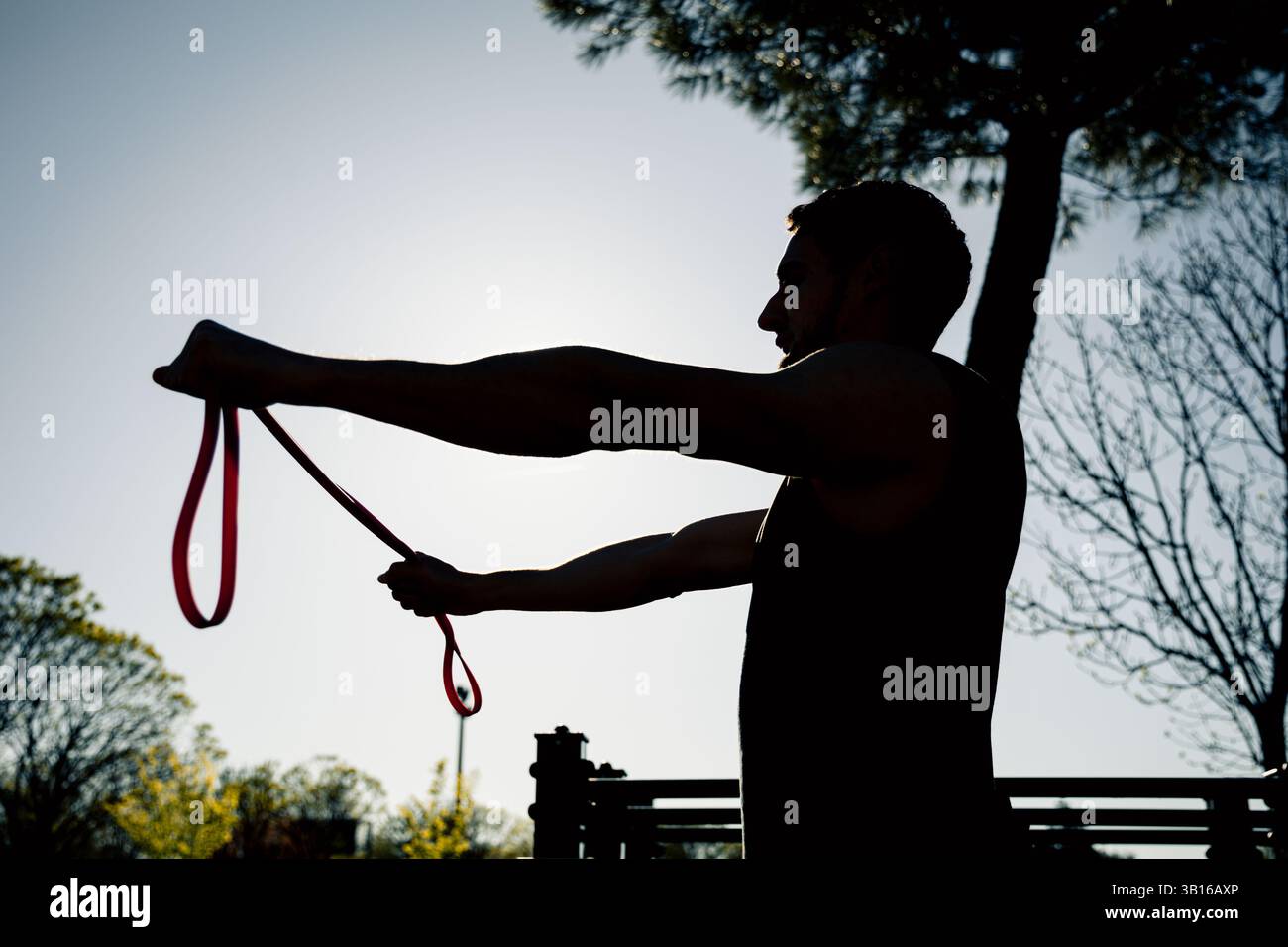 Dans cette image de silhouette puissante, un homme effectue un exercice de bande de résistance à l'extérieur pendant le lever du soleil. Son profil et ses bras étendus créent une ligne solide Banque D'Images