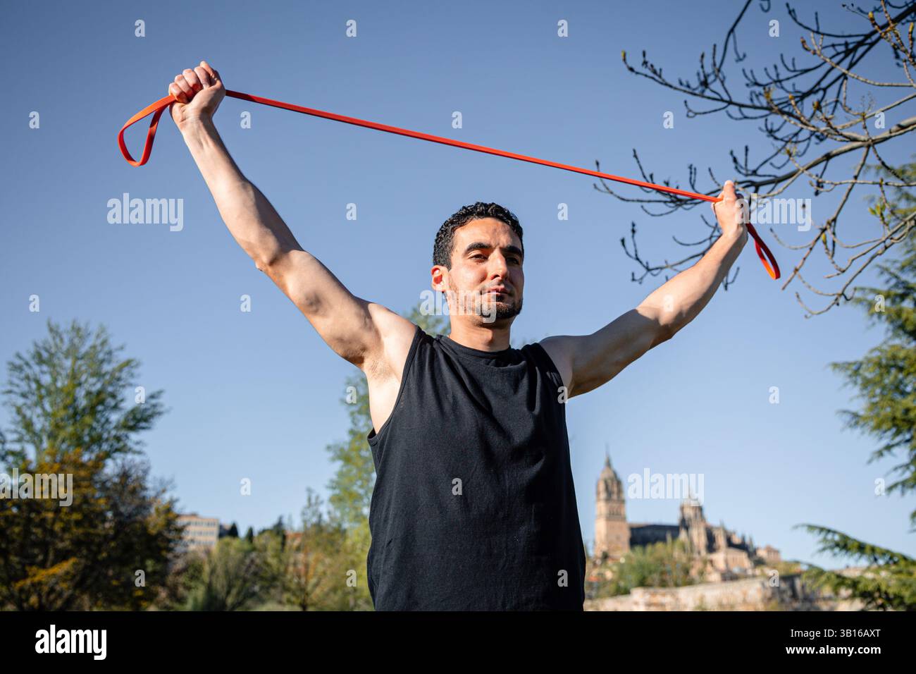Jeune homme étirant la bande de résistance rouge avec les bras tendus pendant l'entraînement de fitness à Salamanque, Espagne avec l'architecture historique en arrière-plan Banque D'Images