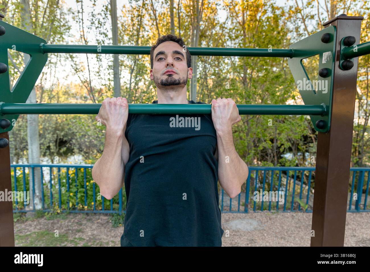 Ajustez l'homme en tenant la position de traction vers le haut avec le menton au-dessus de la barre à l'extérieur, en soulignant la tension du haut du corps, l'effort musculaire et la concentration mentale pendant l'entraînement de force Banque D'Images