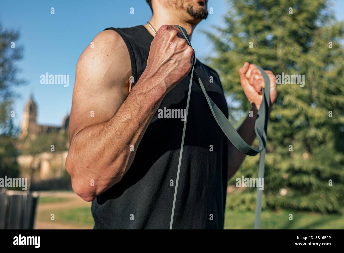 Gros plan de l'homme effectuant des boucles de biceps avec bande de résistance à l'extérieur à Salamanque, Espagne avec cathédrale historique en arrière-plan doux Banque D'Images