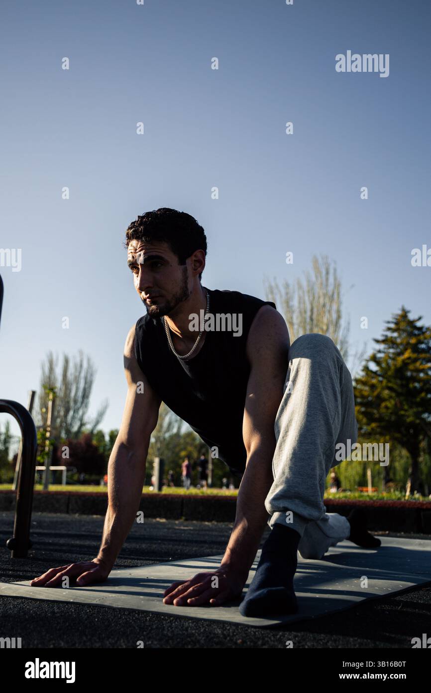 Homme concentré en fente profonde étire dehors sur le tapis d'exercice sous la lumière douce du soleil, démontrant la mobilité, le contrôle et l'intensité de l'échauffement avant l'entraînement Banque D'Images