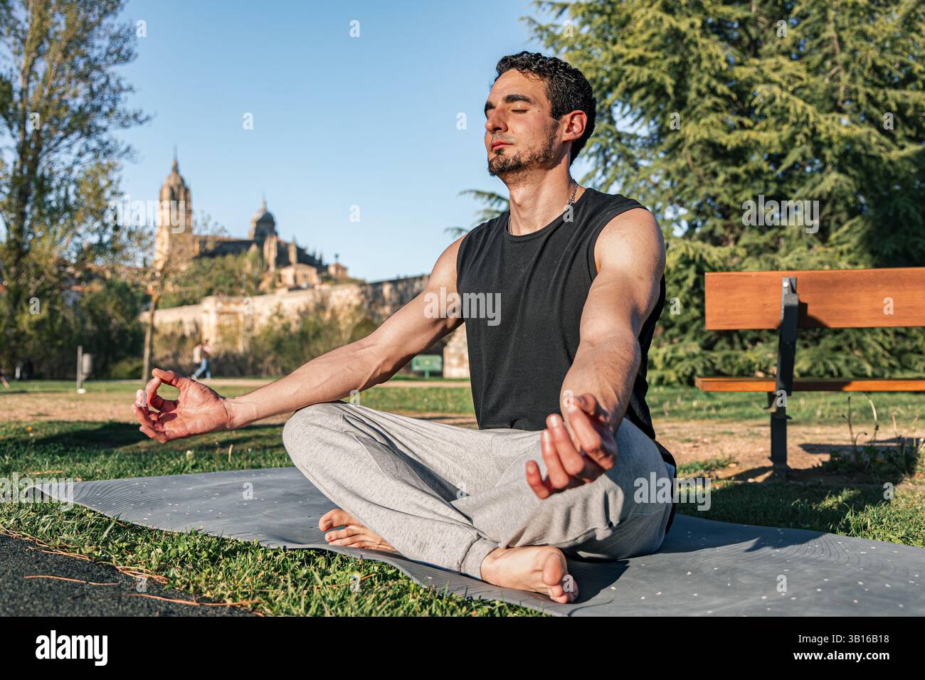 Homme méditant en lotus pose sur tapis à Salamanque, parc espagnol avec cathédrale historique en arrière-plan et les yeux fermés sous la lumière du soleil du matin Banque D'Images