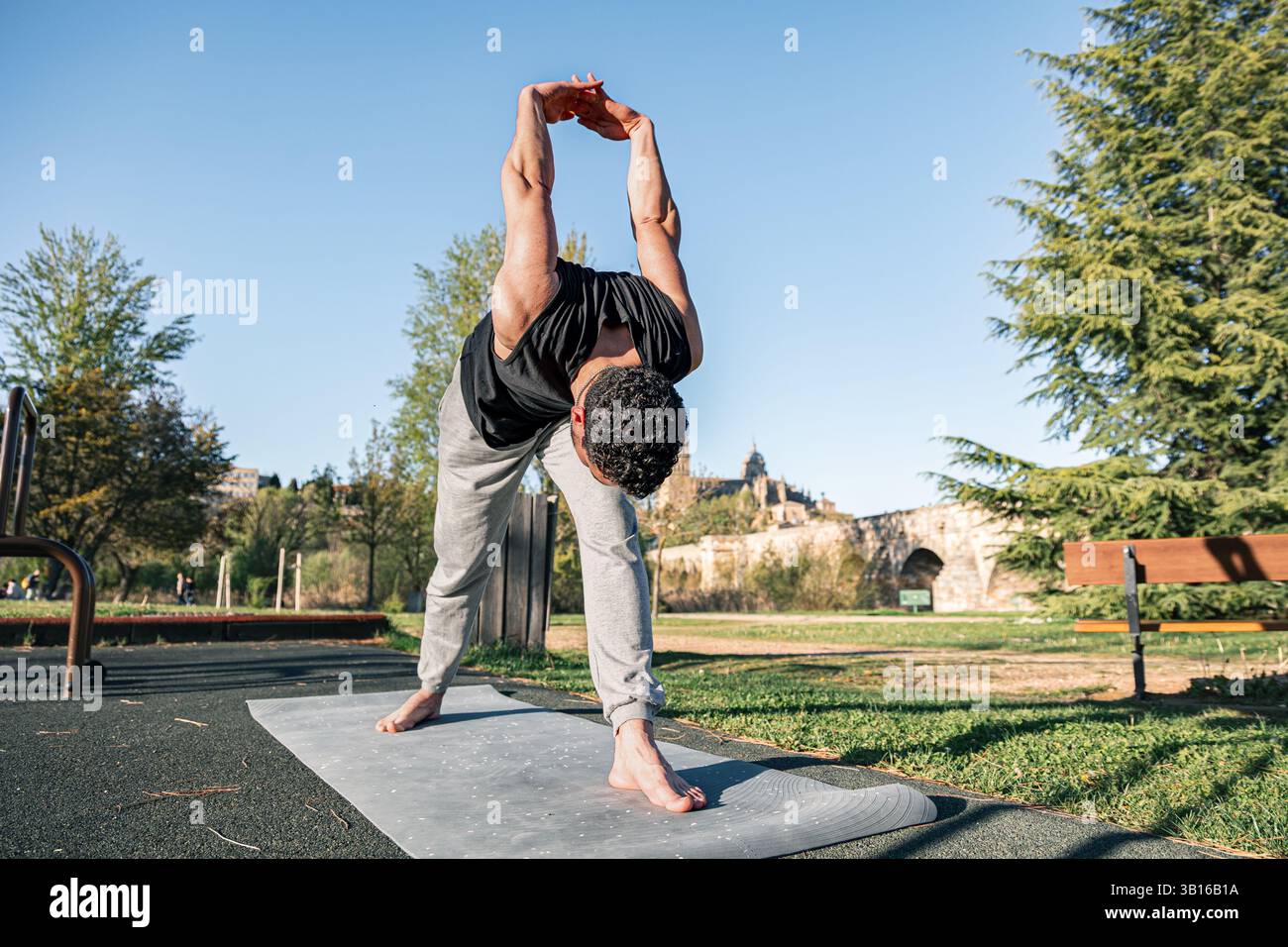 Homme effectuant une pose intense de yoga de flexion avant avec les mains serrées derrière le dos sur tapis à Salamanque, Espagne avec une architecture historique en arrière-plan Banque D'Images