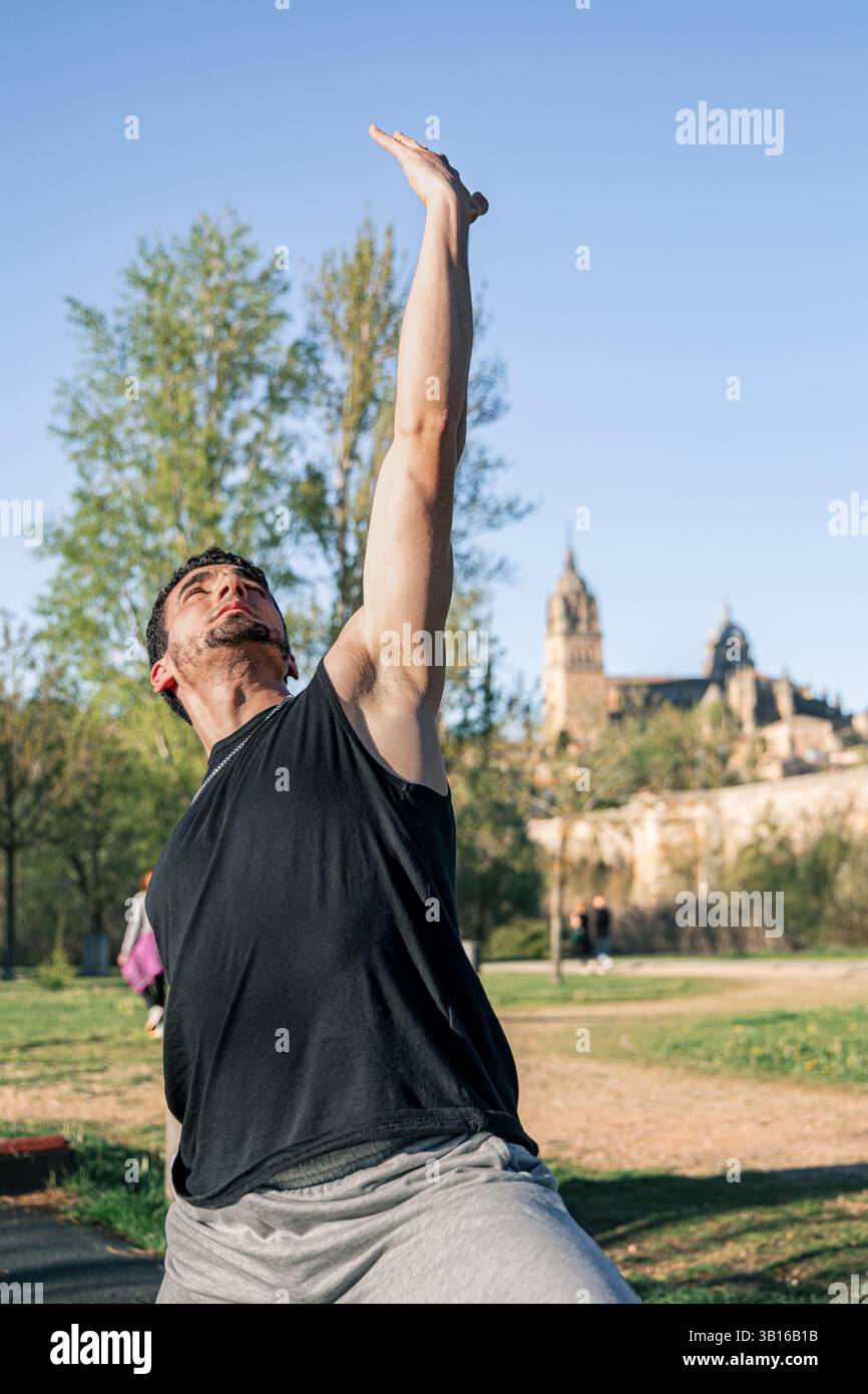 Gros plan d'un homme qui s'étire vers le haut dans une posture de yoga guerrier inversé à l'extérieur à Salamanque, Espagne avec une architecture historique en arrière-plan doux Banque D'Images