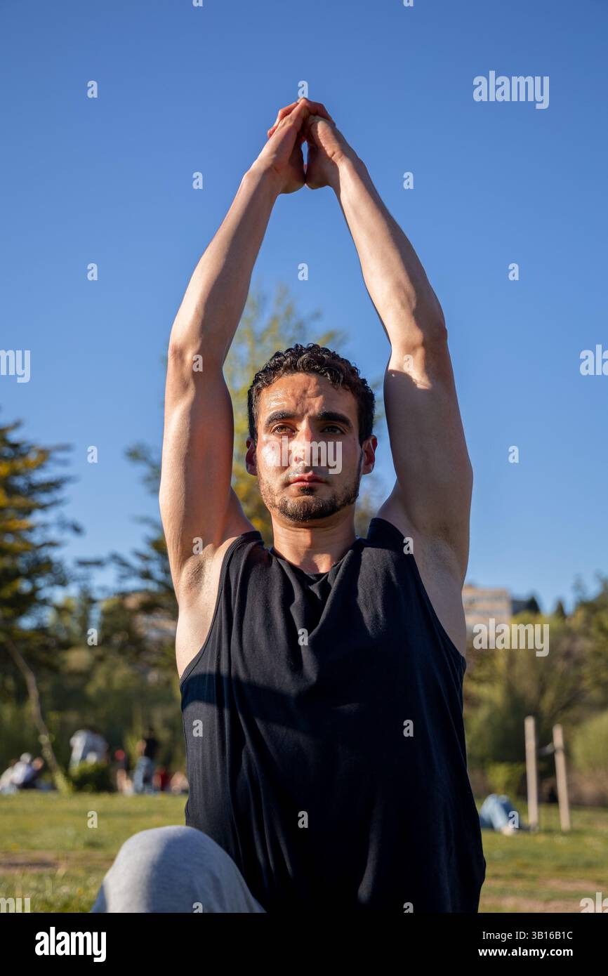 Homme dans l'étirement de yoga vers le haut concentré avec les mains attachées au-dessus de la tête pendant la session en plein air à Salamanque, Espagne sous ciel bleu clair Banque D'Images