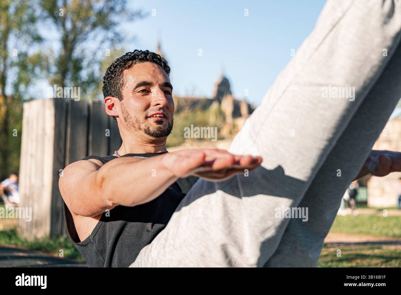Homme en forme effectuant des exercices abdominaux V-sit sur un tapis extérieur, souriant et équilibrant avec les bras et les jambes étendus sous la lumière du jour vive dans le cadre du parc Banque D'Images