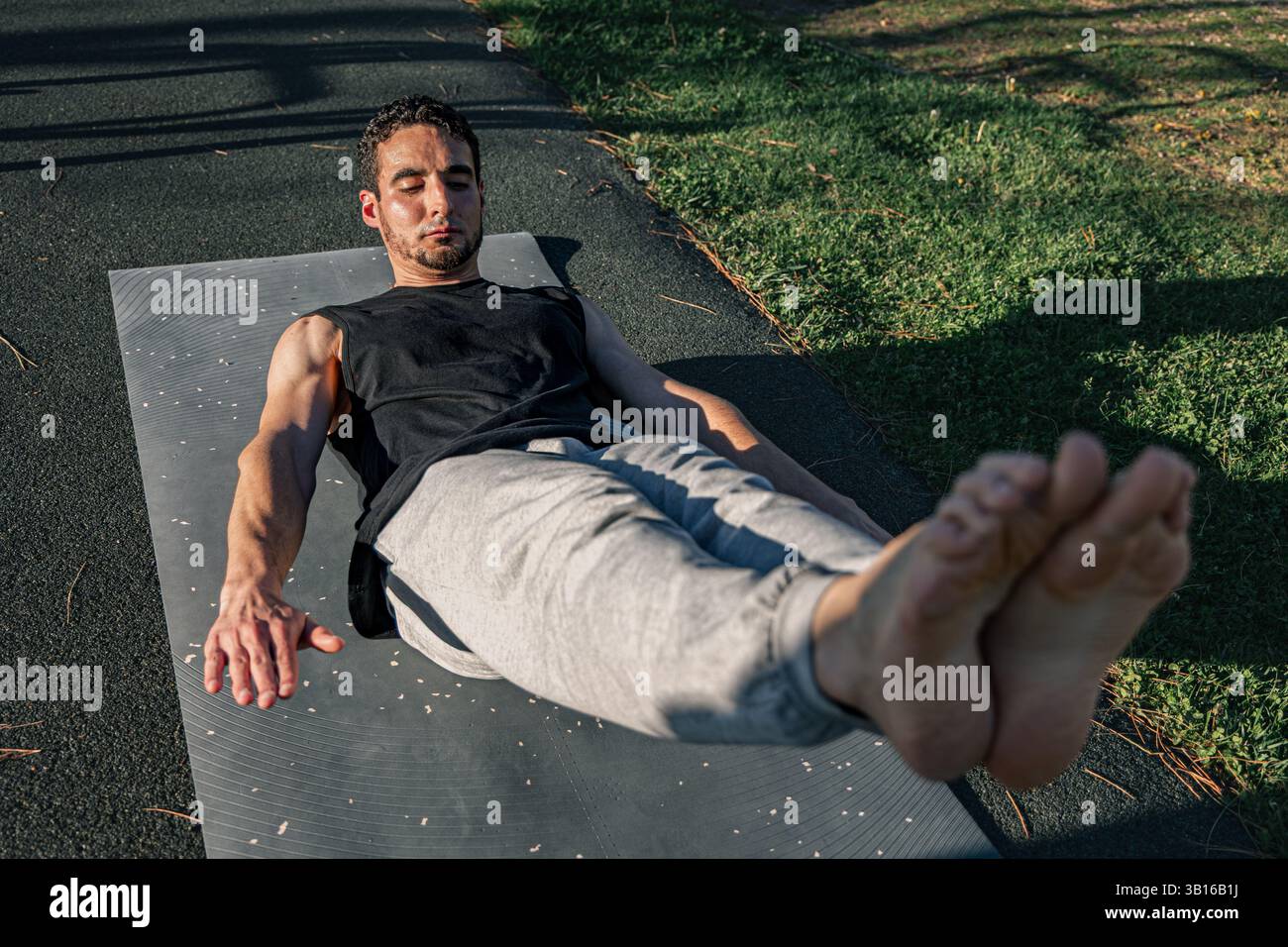 Homme sportif concentré tenant le corps creux pose à l'extérieur sur un tapis, démontrant l'engagement de base et le contrôle du corps pendant la routine de fitness axée sur la force Banque D'Images