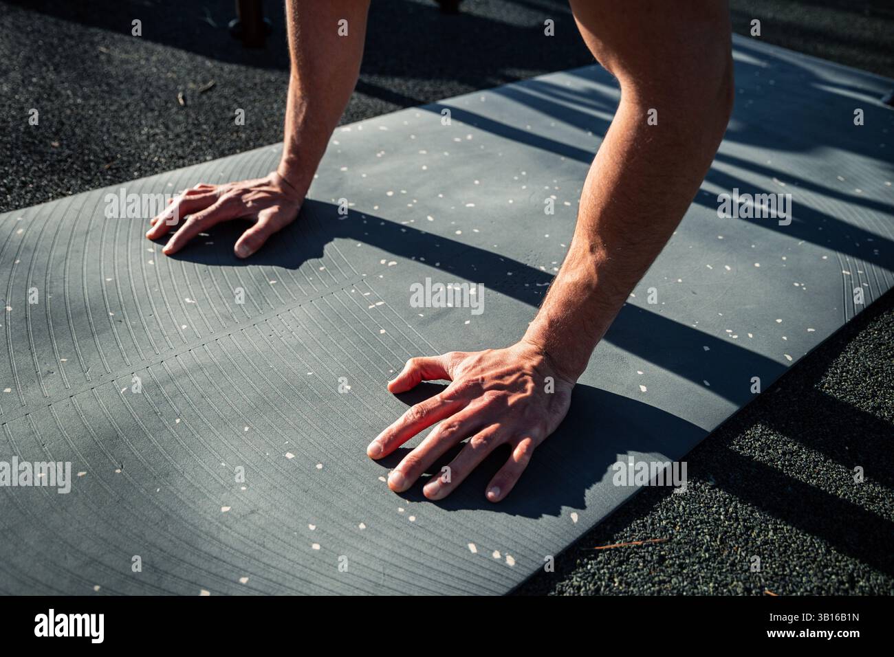 Gros plan des mains masculines sur le tapis d'exercice pendant la position de push-up en extérieur, mettant l'accent sur la force, la forme et l'entraînement physique ciblé à la lumière naturelle Banque D'Images