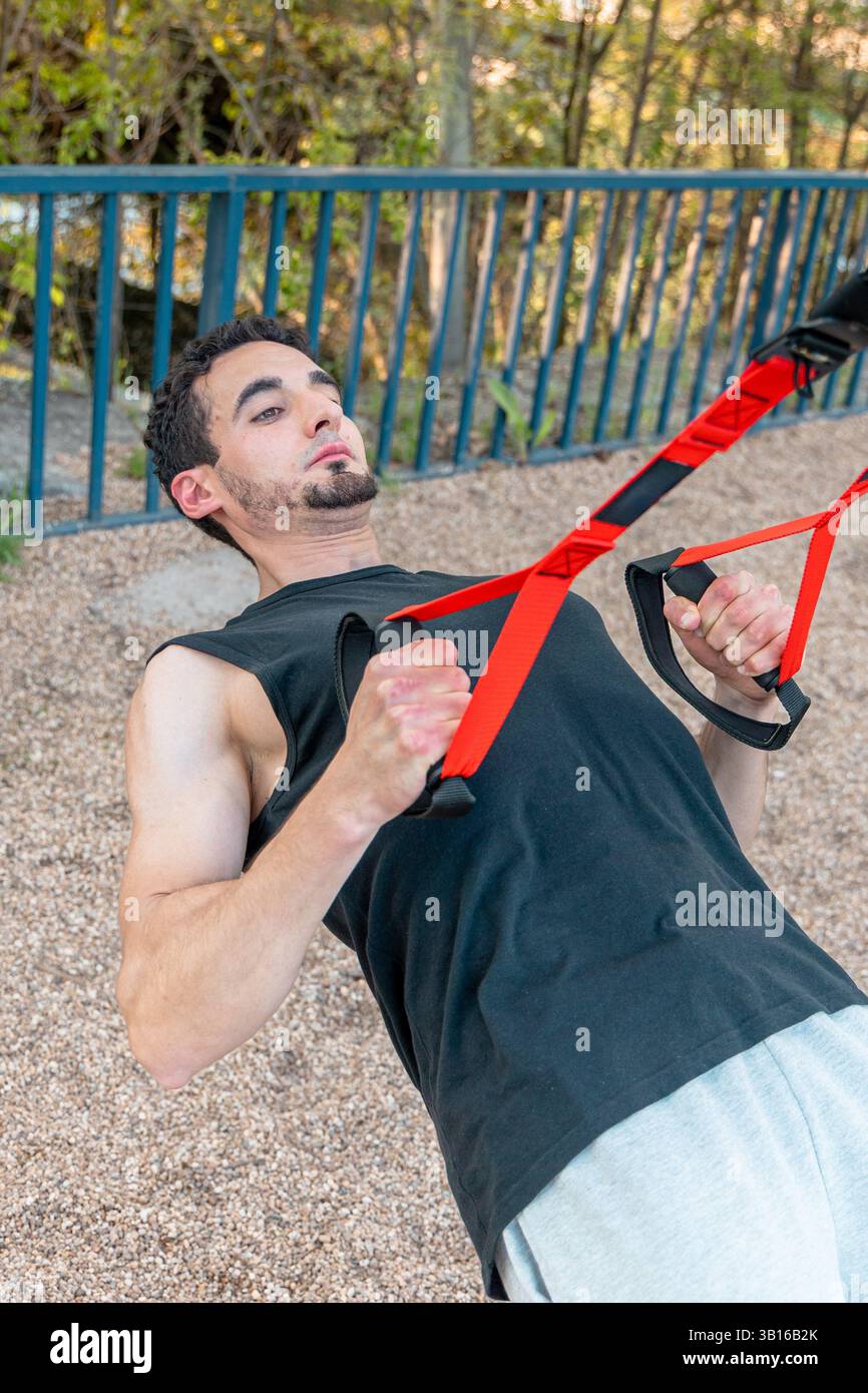 Homme concentré exécutant une rangée de suspension TRX en stationnement avec les bras pliés et la poitrine levée, montrant un exercice de poids corporel contrôlé et un engagement musculaire Banque D'Images