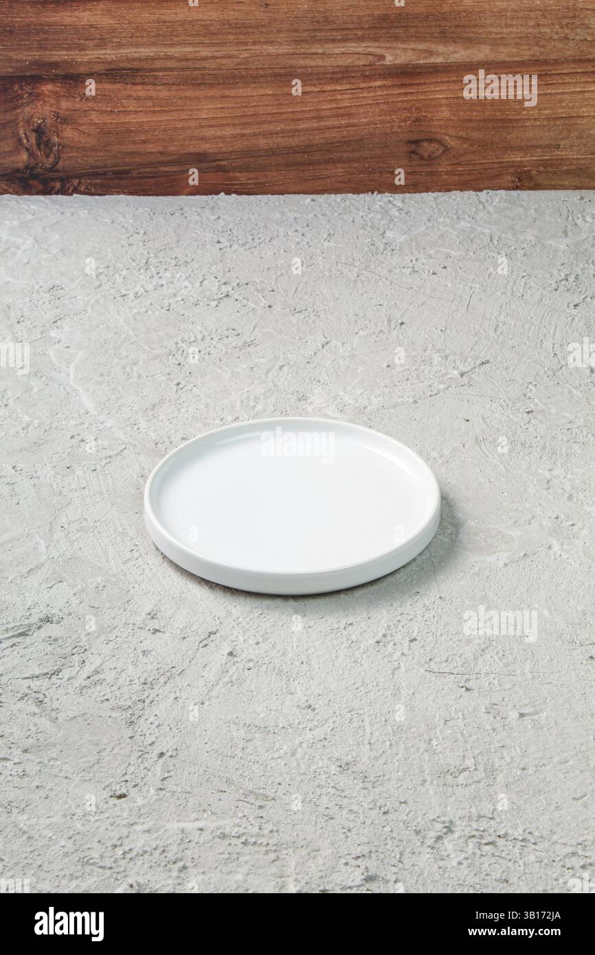 Plaque en céramique blanche minimaliste placée sur une surface en béton texturé avec fond en bois. Idéal pour la photographie alimentaire, les maquettes de vaisselle ou le mod propre Banque D'Images