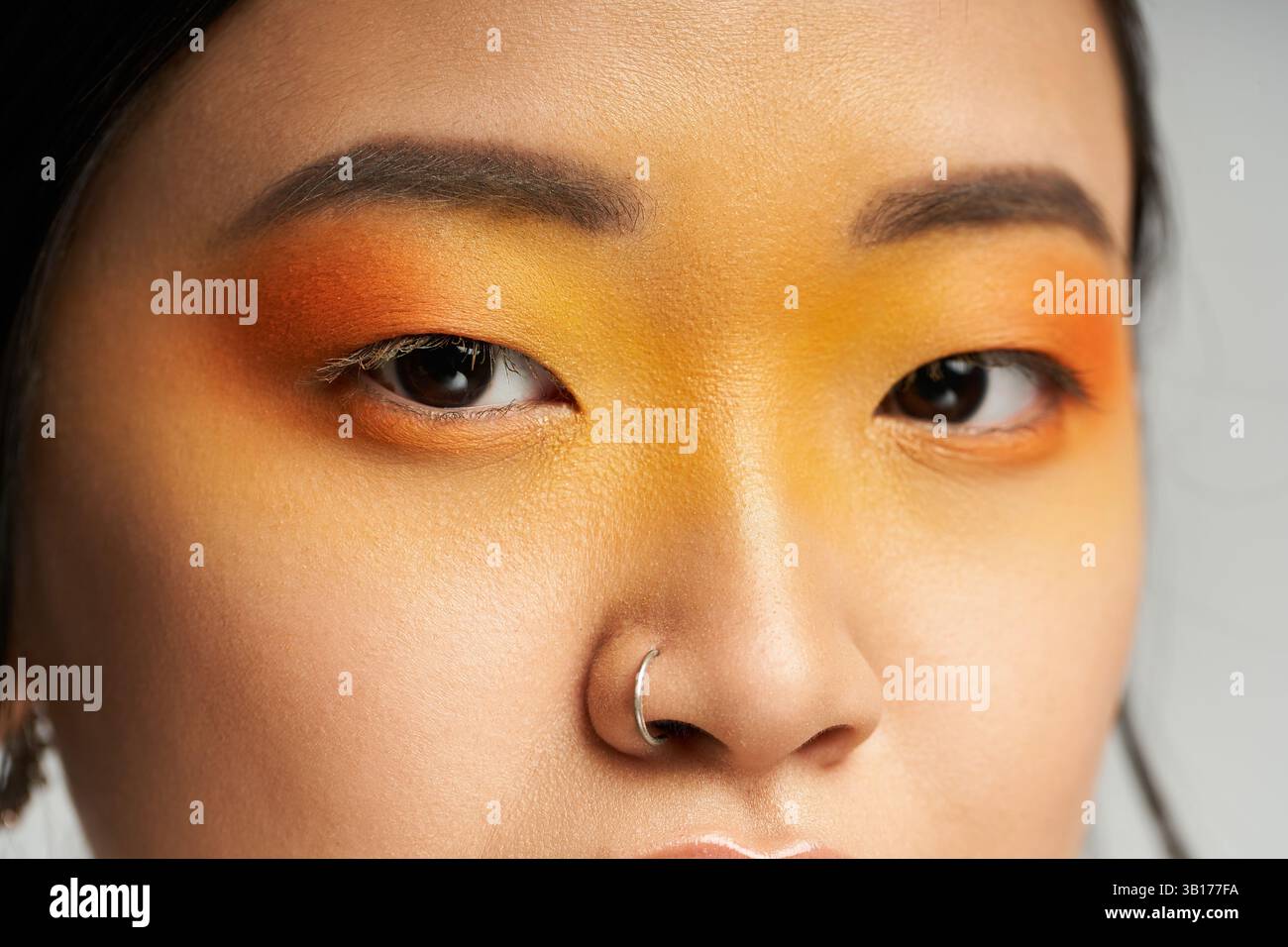 Une jeune femme époustouflante respire le charme avec un maquillage des yeux orange et jaune audacieux en gros plan. Banque D'Images