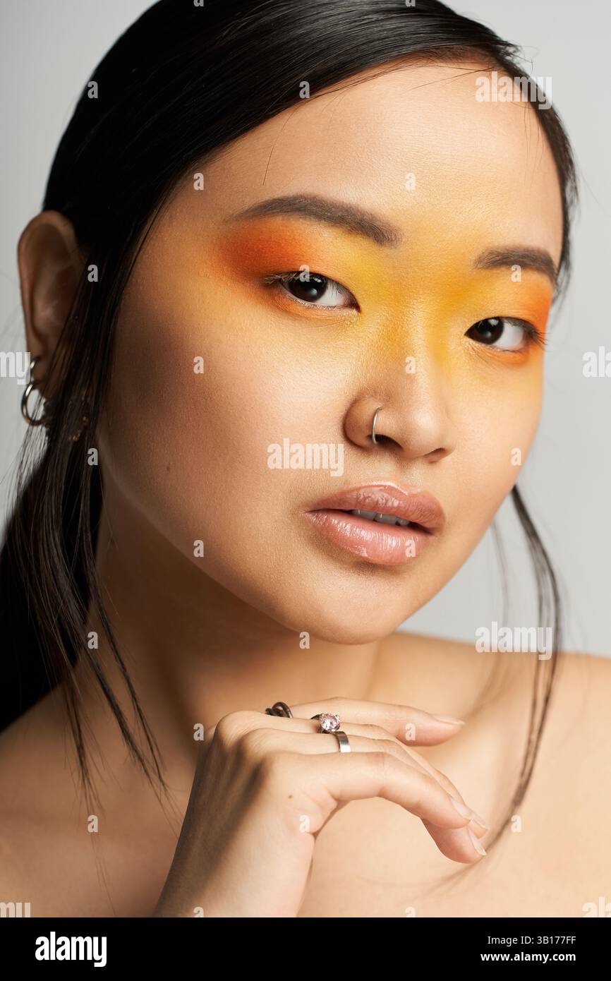 Femme asiatique élégante présente un maquillage orange et jaune audacieux dans un studio. Banque D'Images