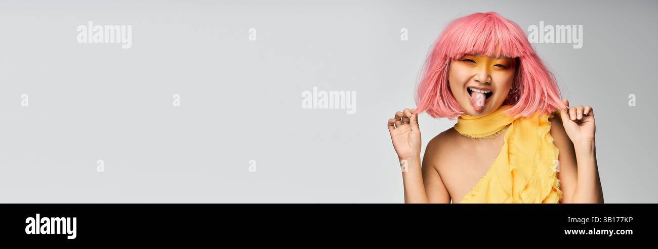 Une jeune femme joyeuse aux cheveux roses pose de manière ludique tout en portant une tenue jaune joyeuse. Banque D'Images