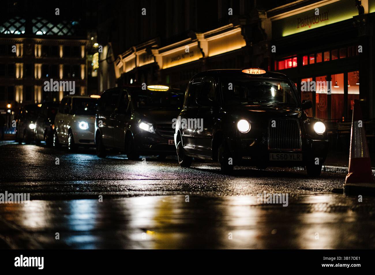Les taxis noirs et autres véhicules attendent dans la circulation sur une rue mouillée de Londres la nuit, éclairés par des phares et des lampadaires. Banque D'Images