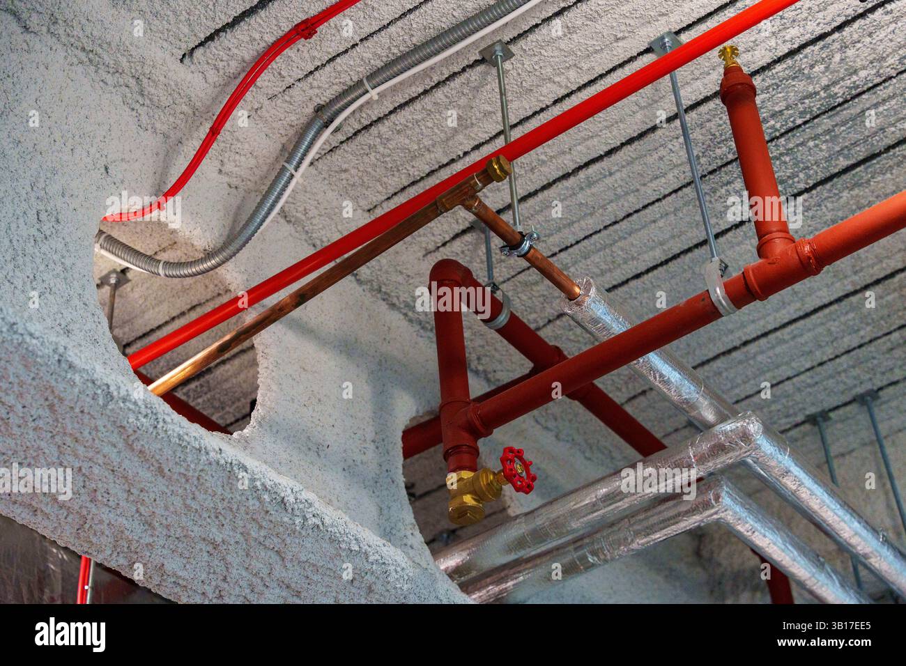 Des tuyaux de gicleurs rouges et des conduits HVAC isolés sont installés sous un plafond en béton texturé dans un bâtiment, mettant en valeur l'utilité industrielle. Banque D'Images