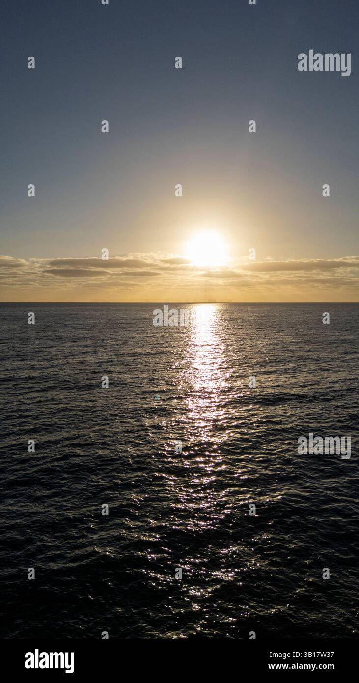Le soleil se couche sur l'océan, projetant une lueur chaude sur l'eau. Le ciel est d'un bleu profond Banque D'Images