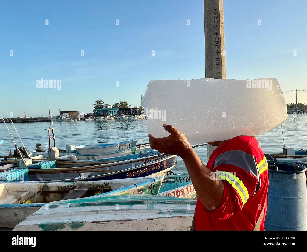 Homme transportant un morceau de glace à prendre sur un bateau pour stocker la prise du jour, El Cuyo, Yucatan, Mexique . La chaleur intense et le réchauffement climatique rendent cela essentiel pour que les poissons ne se gâtent pas Banque D'Images