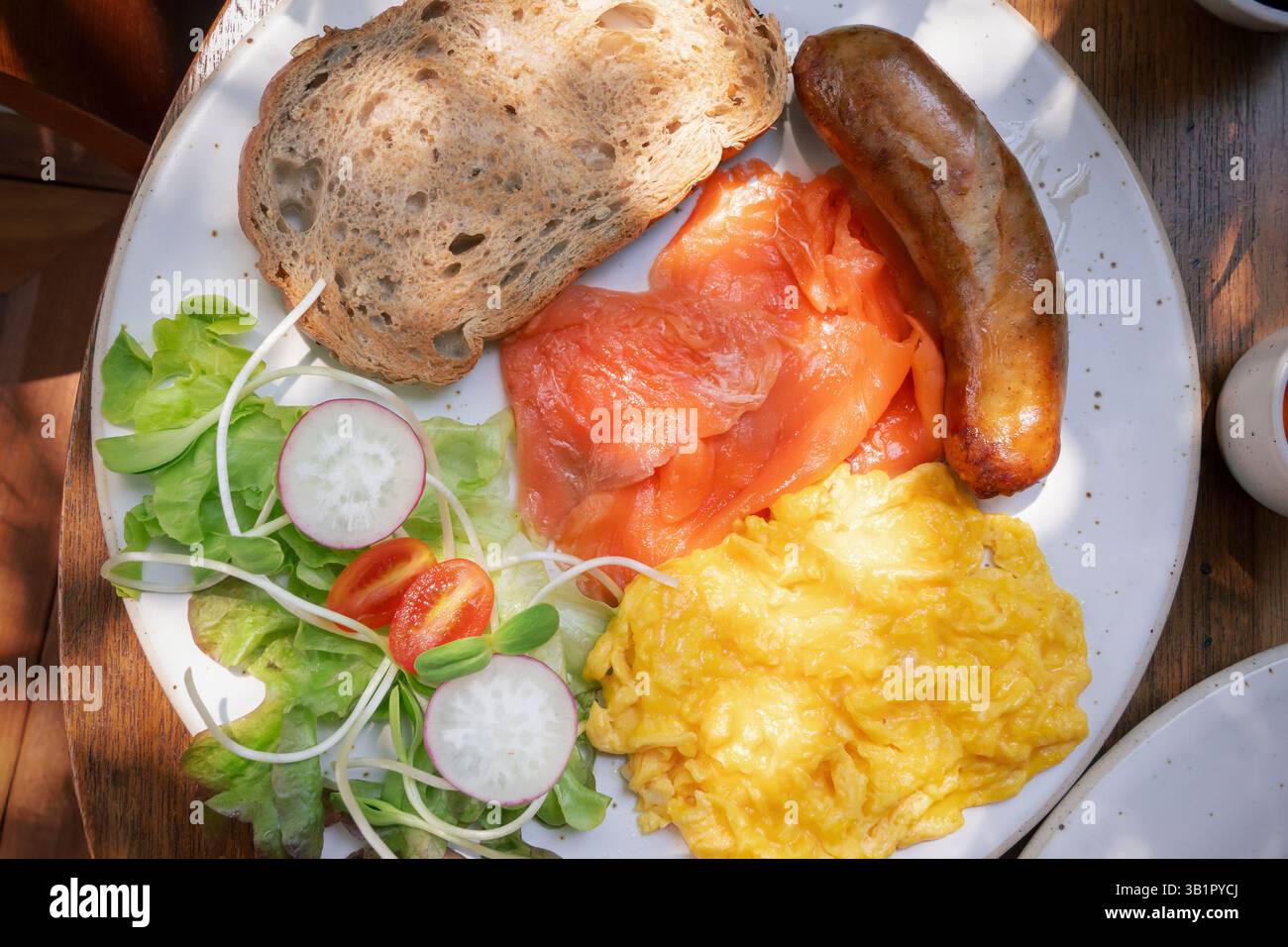 Un copieux plateau de petit-déjeuner présente un assortiment vibrant de saumon fumé, d'œufs brouillés moelleux, une saucisse juteuse et des légumes frais, y compris lea Banque D'Images