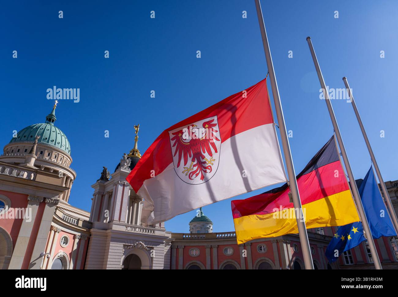 Potsdam, Allemagne. 26 avril 2025. Le drapeau de l'État de Brandebourg flotte en Berne dans la cour intérieure du bâtiment du parlement de l'État sur la toile de fond de l'église Nicolas sur l'Alter Markt. En raison de la mort du pape François et du deuil national associé, des drapeaux de deuil ont également été commandés pour les bâtiments officiels du Brandebourg aujourd'hui. Crédit : Soeren Stache/dpa/Alamy Live News Banque D'Images