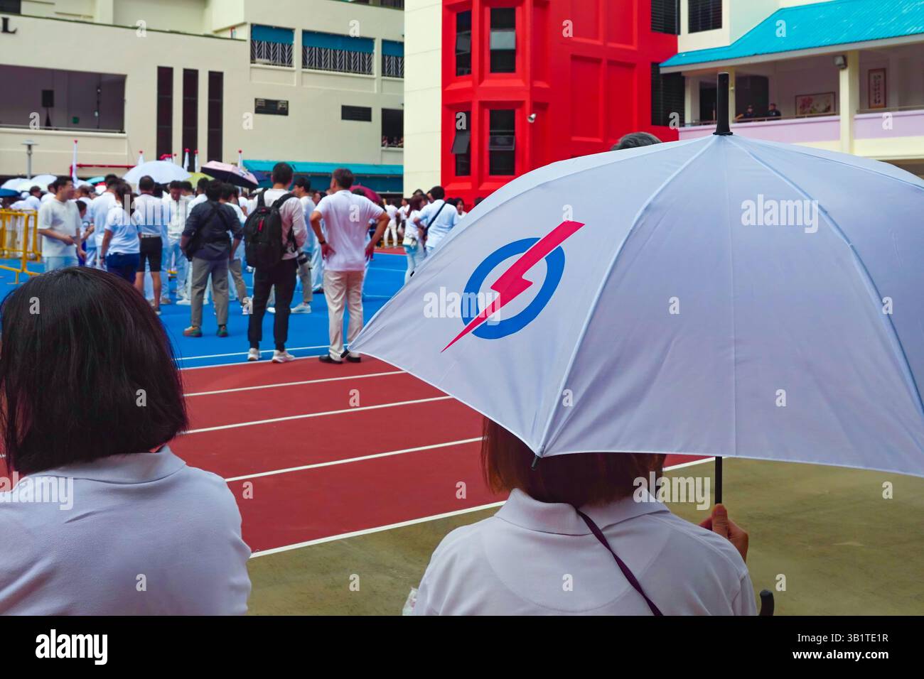 Singapour 2025 avr23 - jour de la nomination aux élections générales. Un partisan du PAP avec parapluie regarde les gens se rassembler à l'école de Chongfu, attendant le Ret Banque D'Images