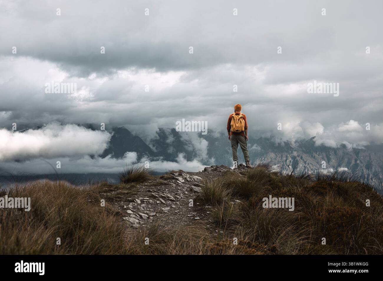 Randonneur en équipement lumineux face aux montagnes escarpées et Moody Sky, aventure, solitude et beauté naturelle, contemplation dans la nature sauvage isolée. Banque D'Images Randonneur en équipement lumineux face aux montagnes escarpées et Moody Sky, aventure, solitude et beauté naturelle, contemplation dans la nature sauvage isolée. Banque D'Images