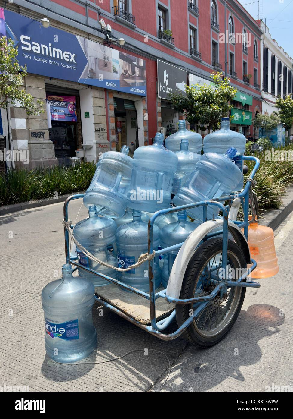 Beaucoup de gens dans la ville de Mexico considèrent encore que l'eau du robinet n'est pas potable. Par conséquent, les camions manuels à trois roues se déplacent dans les quartiers pour recueillir les vides et livrer des bouteilles d'eau pleines. Cela crée une mini économie pour de nombreux pauvres impliqués dans ce métier de distribution et permet le recyclage des grosses bouteilles en plastique qui sont renvoyées aux entreprises pour être nettoyées, désinfectées et rechargées professionnellement dans des normes d’hygiène strictes Banque D'Images