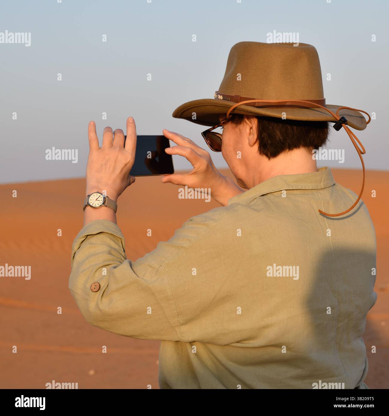 Désert de Rub Al Khali, Sultanat d'Oman. Femme en chapeau de cow-boy prend une photo des dunes dans le désert de Wahiba Sands au lever du soleil, péninsule arabique Banque D'Images