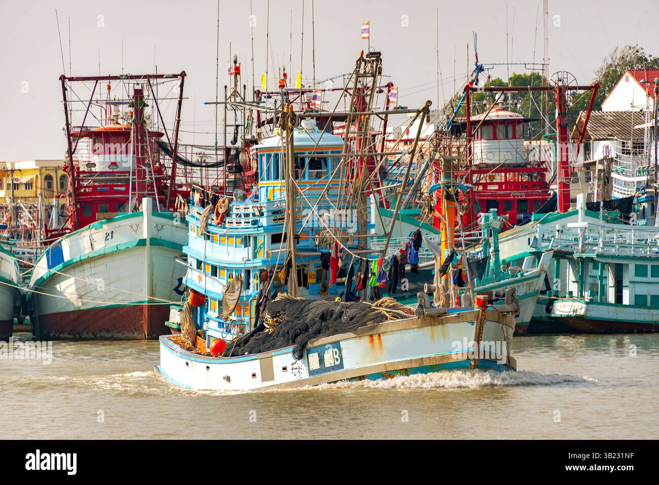 Port de pêche animé : de nombreux bateaux de pêche colorés avec gréement et filets ancrés dans une voie navigable. Banque D'Images