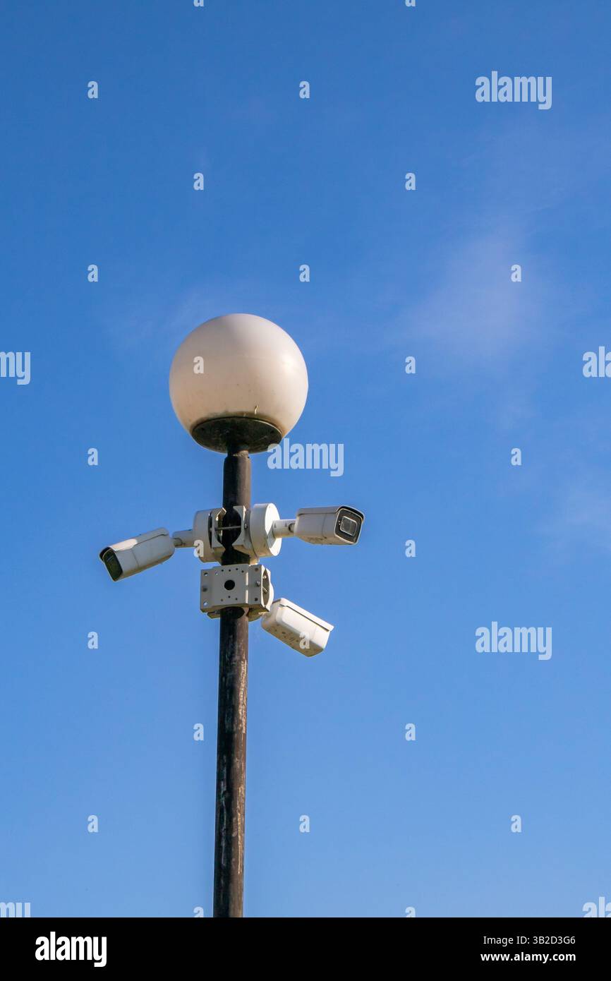 Un lampadaire avec une ampoule blanche ronde est monté sur un poteau, entouré de plusieurs caméras de surveillance. Le ciel bleu clair sert de toile de fond, indi Banque D'Images