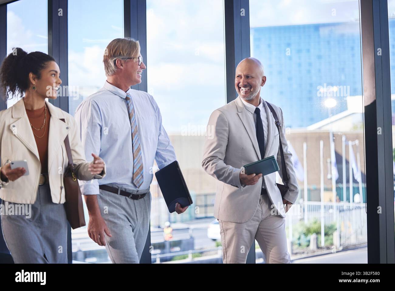 Les affaires, les gens et la marche avec les associés dans le bureau, heureux et parler dans la construction du lieu de travail. Ensemble, discussion et collaboration avec l'entreprise Banque D'Images