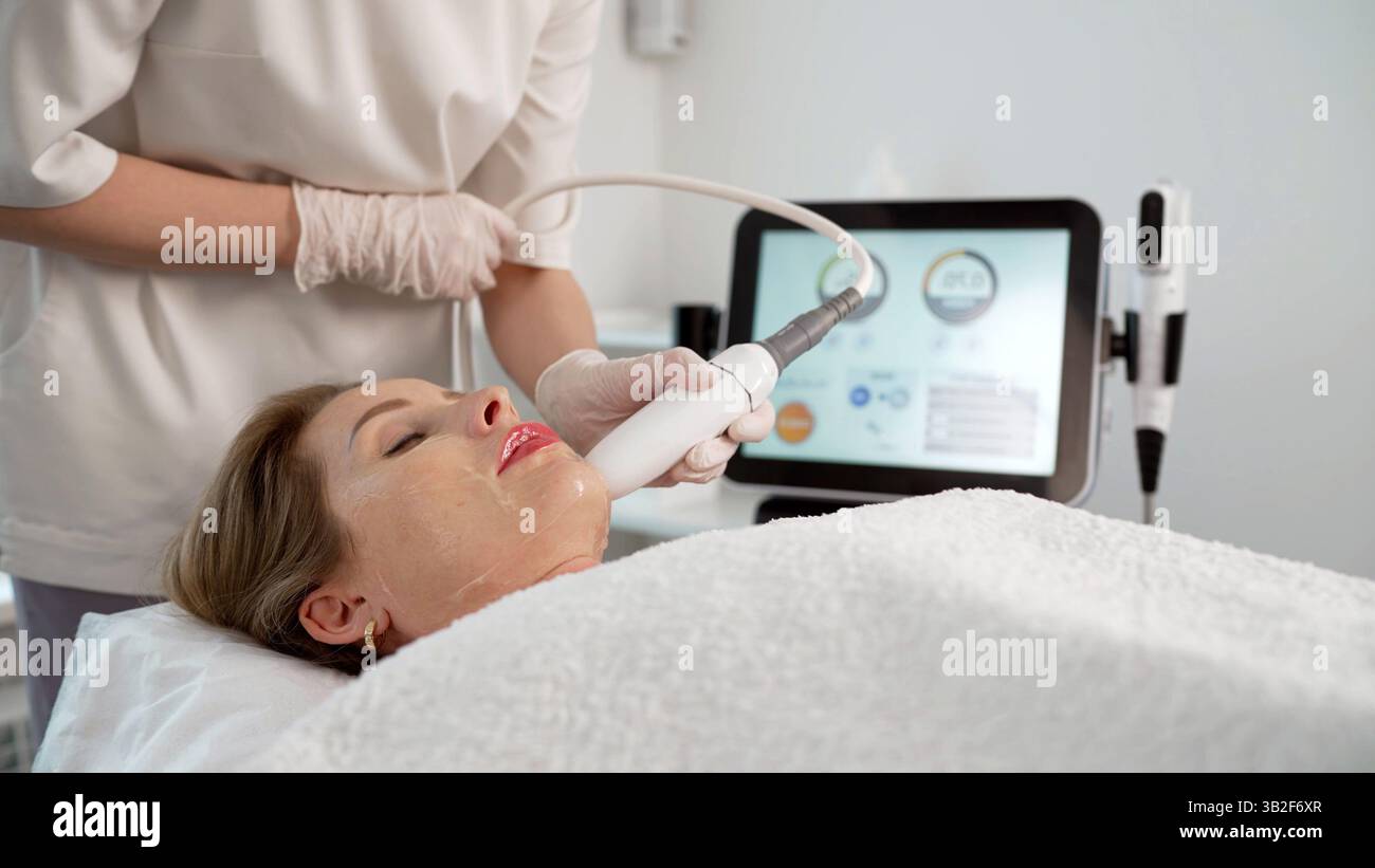 Esthéticienne appliquant un appareil non chirurgical de lifting du visage et de resserrement de la peau sur une femme mature, améliorant sa beauté et rajeunissant sa peau Banque D'Images