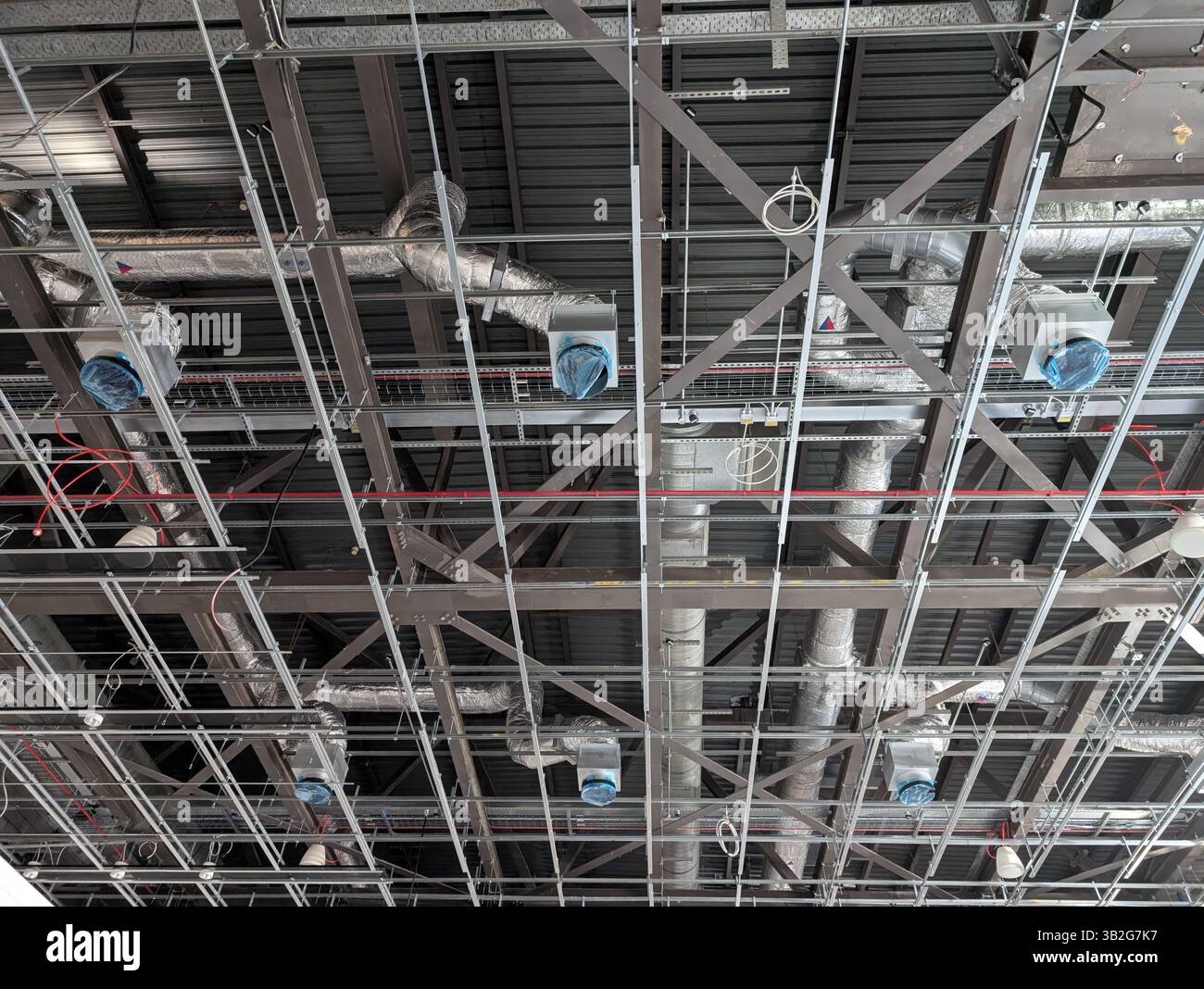 Plafond exposé industriel en construction, avec gaines HVAC, câblage électrique, tuyauterie et cadre de grille de plafond suspendu. L'image sho Banque D'Images