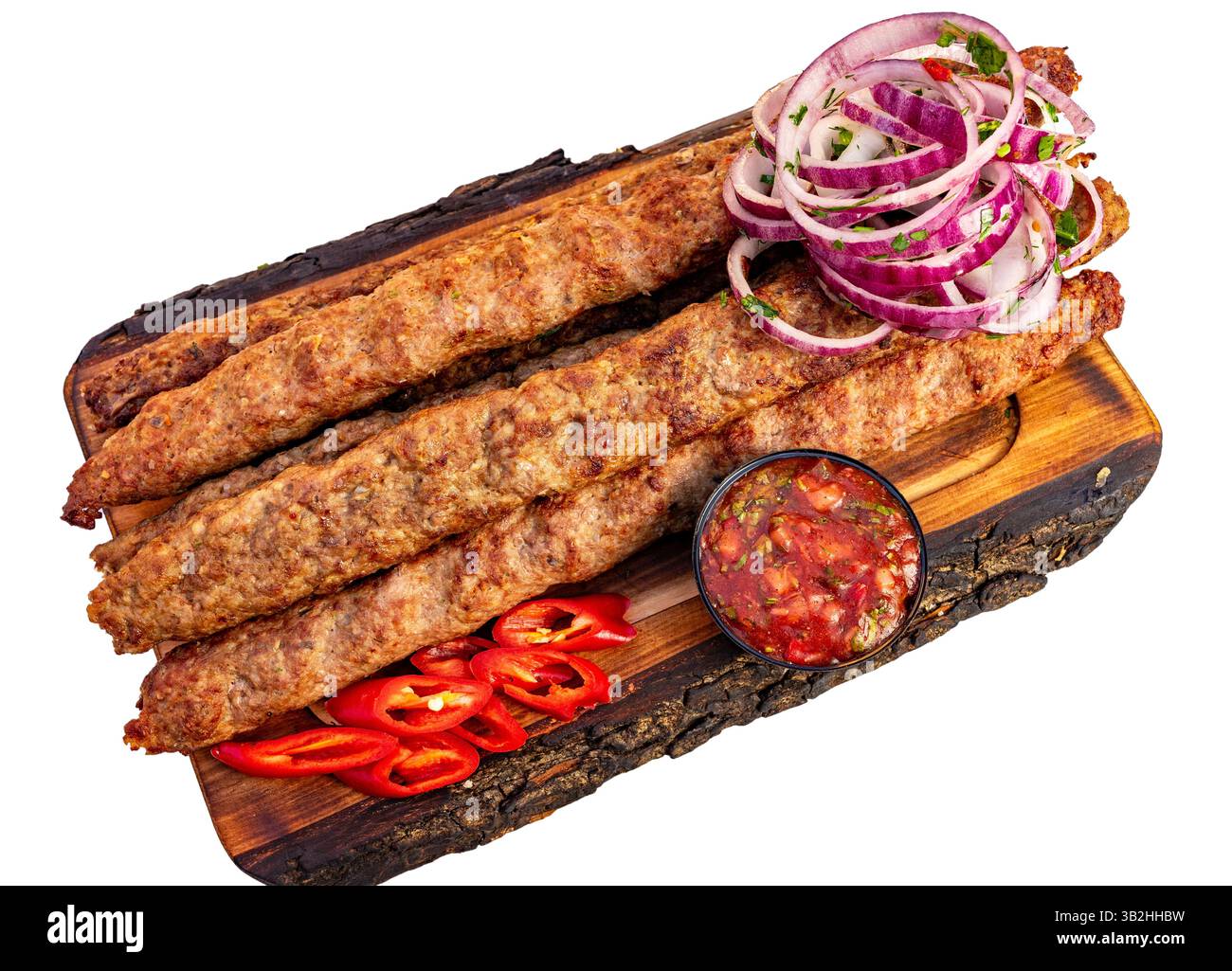 Les kebabs juteux sont parfaitement grillés et présentés sur un plateau en bois. Des tranches d'oignon rouge et des piments frais accompagnent le plat, à côté d'un smal Banque D'Images