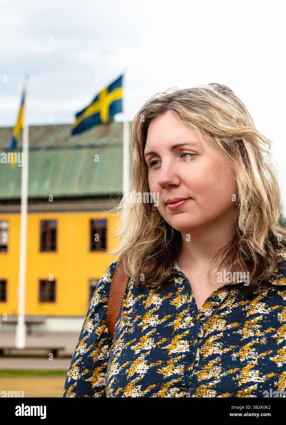 Une femme pose soigneusement avec les drapeaux suédois et ukrainien en vue, face à un bâtiment coloré en Suède pendant une journée d'été ensoleillée. Banque D'Images