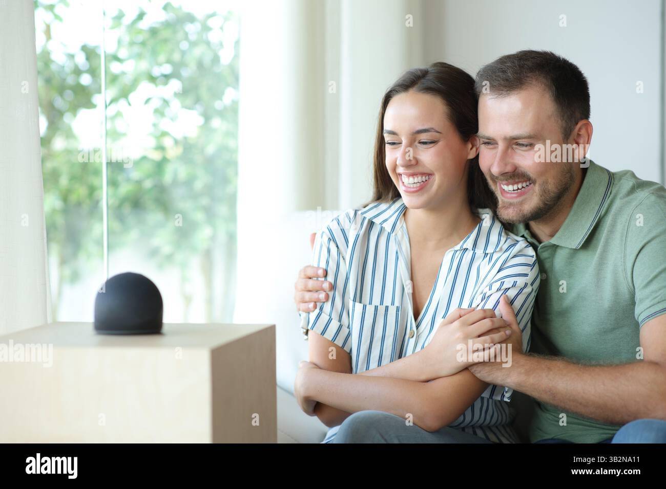 Heureux couple appréciant de regarder la nouvelle enceinte intelligente assis sur un canapé à la maison Banque D'Images