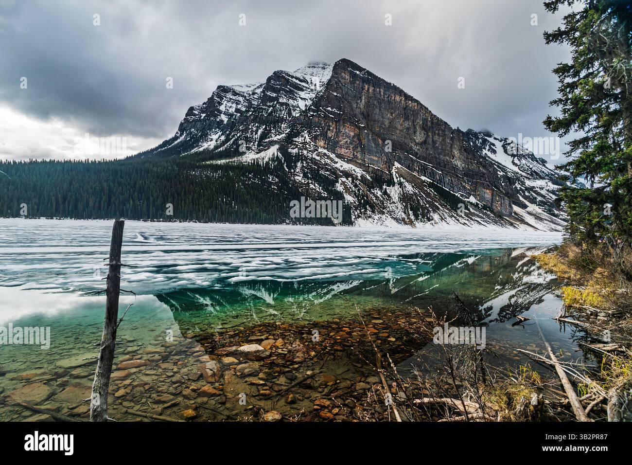 Une vue imprenable sur le lac Louise dans le parc national Banff, Alberta, Canada, illustre la transition de l'hiver au printemps. Le lac partiellement gelé refl Banque D'Images