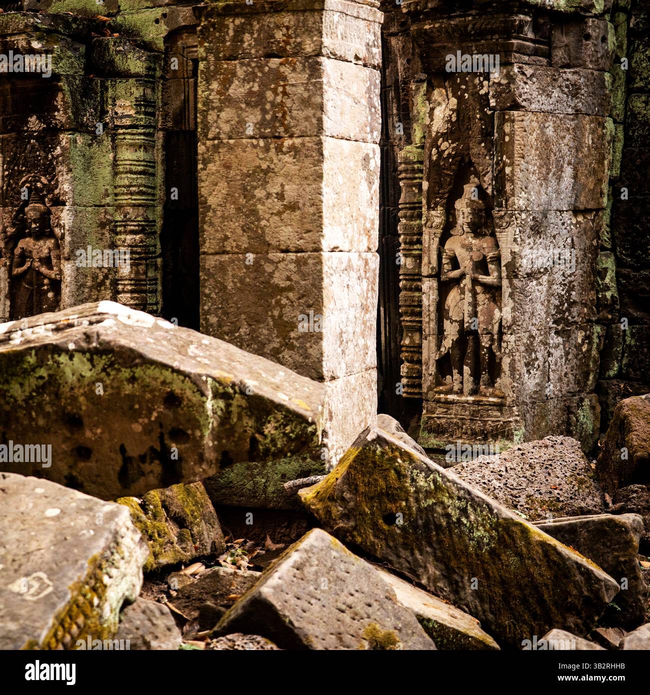 Anciennes ruines en pierre avec des sculptures complexes, partiellement recouvertes de mousse et entourées de rochers tombés. La scène évoque un sens de l'histoire et du mystère Banque D'Images