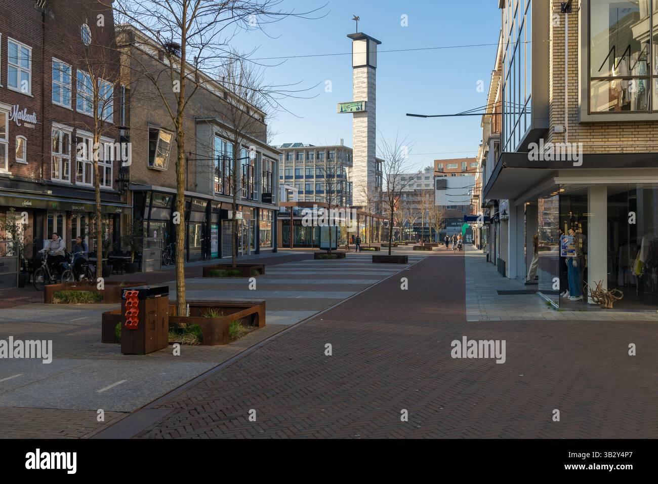 Rue moderne de la ville européenne avec des magasins, des gens, et une tour de l'horloge centrale par temps clair dans un cadre urbain paisible. Hengelo, pays-Bas. 28 mars Banque D'Images