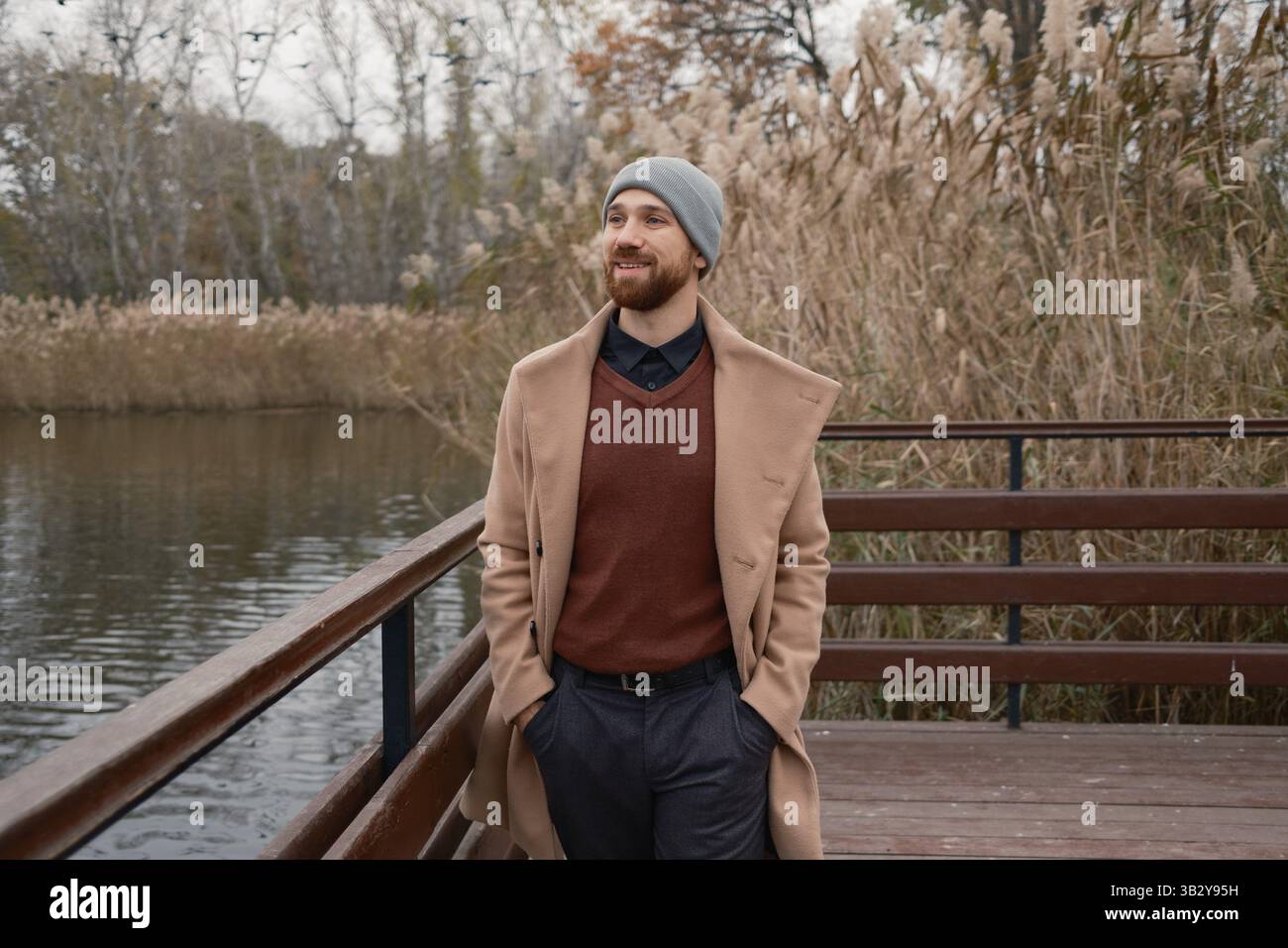 Homme en tenue d'hiver élégante debout sur un pont au-dessus de l'eau calme Banque D'Images