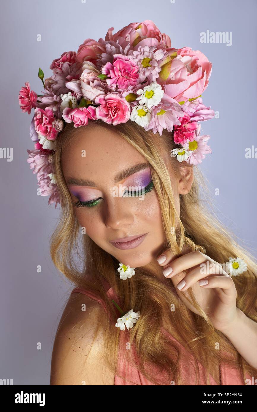 femme ornée d'une couronne de fleurs roses et de regards de maquillage vibrants réfléchis vers le bas. Elle met en valeur des boucles douces dans un studio, créant un an serein Banque D'Images