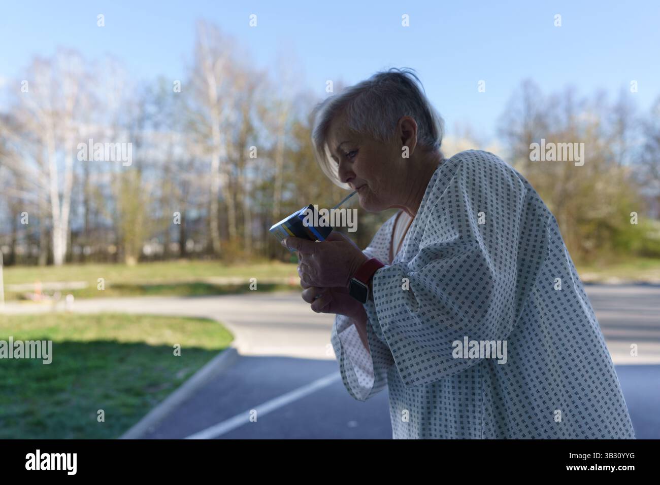 Patiente en robe d'hôpital fumant en dehors d'un établissement médical. Banque D'Images