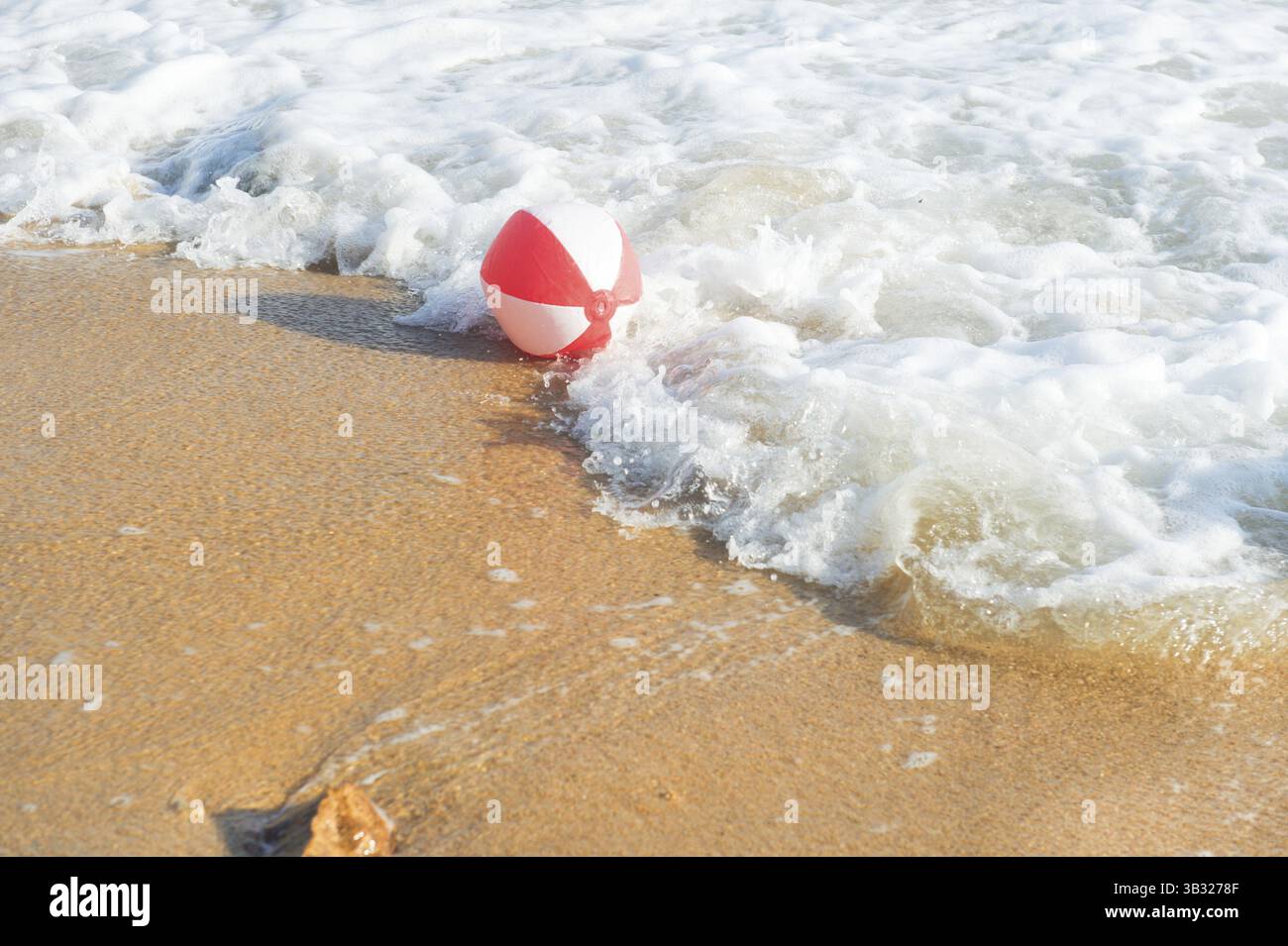 Ballon de plage rouge et blanc jouant avec les vagues et la mer à la plage Banque D'Images