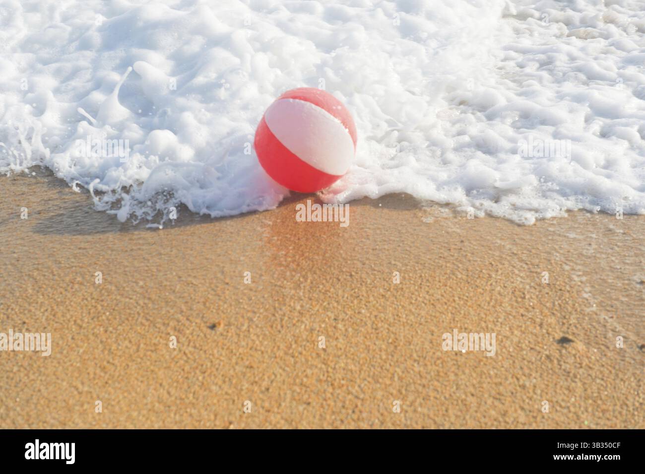 Ballon de plage rouge et blanc jouant avec les vagues et la mer à la plage Banque D'Images